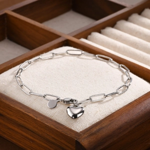 Gros plan d'un bracelet chaîne trombone argenté avec breloque cœur sur un support lin