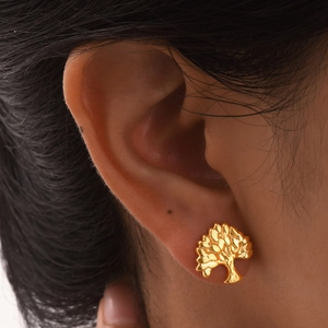 Close-up of a golden tree of life stud earring worn on the ear showing polished details