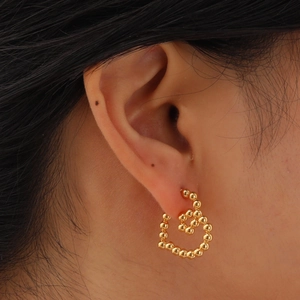Goldene Herzohrstecker aus kleinen Metallperlen am Ohrläppchen eines Models