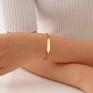 Detailed view of a gold-plated stainless steel bar bracelet worn on a woman's wrist