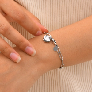 Bracelet en acier inoxydable argenté avec breloque cœur porté sur fond en tricot