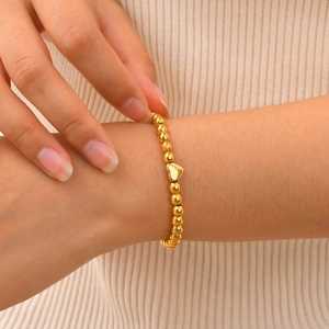 Elegant gold beaded stainless steel heart bracelet on female wrist with cozy beige fabric