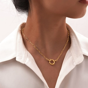 Detail shot of a golden paperclip chain necklace with a large circular spring clasp