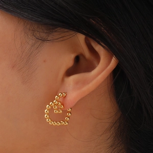 Makroaufnahme goldener Herzohrstecker aus Edelstahlperlen am Ohr eines Models