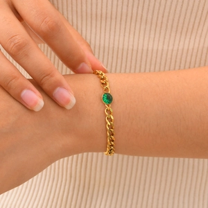 Dettaglio del bracciale a catena cubana dorata con zircone verde tondo su sfondo in maglia