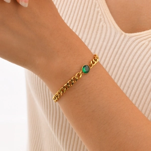 Dettaglio del bracciale a catena cubana dorata con zircone verde sul polso