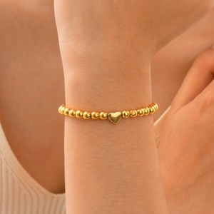 Close-up of polished gold beaded bracelet featuring a heart charm on a female wrist