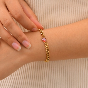 Dettaglio di un bracciale a catena cubana dorata con zircone rosso tondo sul polso