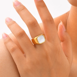 Macro shot of a chunky gold square signet ring with a white mother of pearl inlay on finger