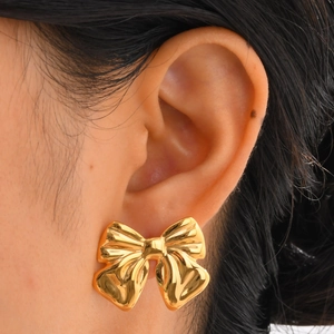 Vue macro de boucles d'oreilles nœud dorées avec texture polie sur l'oreille du mannequin