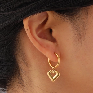Boucles d'oreilles créoles avec pendentif cœur doré portées par un mannequin élégant