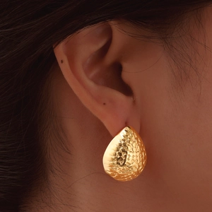 Gros plan de boucles d'oreilles goutte dorées avec texture métallique martelée sur l'oreille