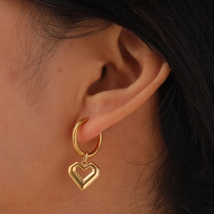 Gros plan d'une femme portant des boucles d'oreilles cœur dorées au design géométrique