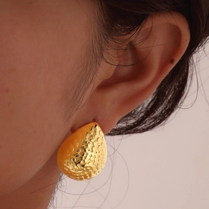Gros plan de boucles d'oreilles goutte dorées avec texture martelée portées par un mannequin