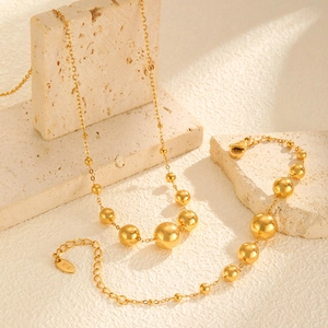 Ensemble collier et bracelet dorés à billes dégradées sur un bloc de pierre texturé