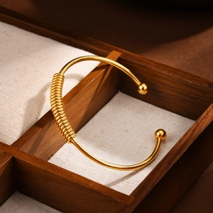 Gold stainless steel open bangle with spring coil detail on dark wood jewelry box display