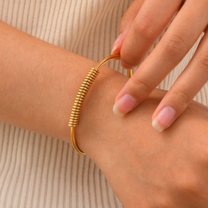 Elegant gold stainless steel spring element open bangle worn on wrist with white knitwear