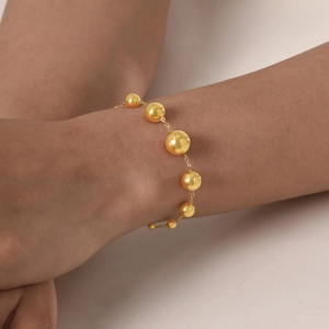 Détail d'un bracelet doré pour femme avec des perles à effet miroir sur une chaîne fine