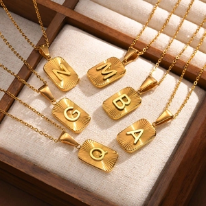Detailed view of six gold rectangular initial pendants with radial texture on linen tray