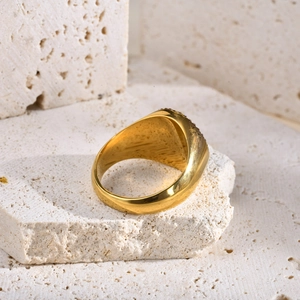 Détail d'une bague chevalière dorée ornée de zircons sur un support en pierre naturelle