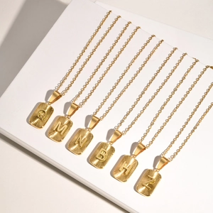 Detailed close-up of gold rectangular pendant necklaces with engraved solar texture letters