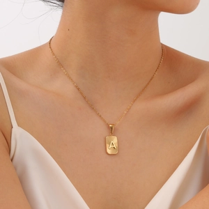 Close-up of gold geometric square pendant with letter A engraving and sunburst texture