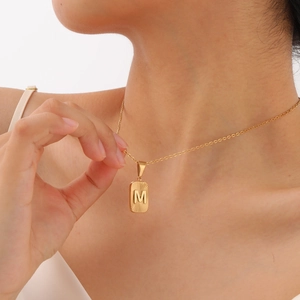 Detail of gold rectangular pendant featuring letter M and sunburst texture on a link chain