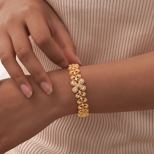 Detail of a gold flower bracelet with sparkling zircons worn by a model on a beige background