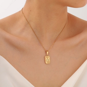 Close-up of gold-plated square pendant with sunburst texture and M initial engraving