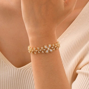 Detail of a gold flower bracelet with cubic zirconia on a warm knit sleeve background