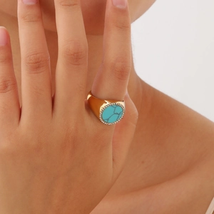 Détail de la bague dorée avec pierre turquoise entourée de zircons cubiques blancs