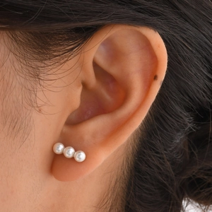 Close-up of minimalist triple white pearl stud earrings on ear for a modern look