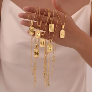 Detail of gold stainless steel rectangular pendant necklaces with engraved letters