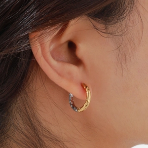 Détail macro de boucles d'oreilles créoles bicolores avec texture martelée portées à l'oreille