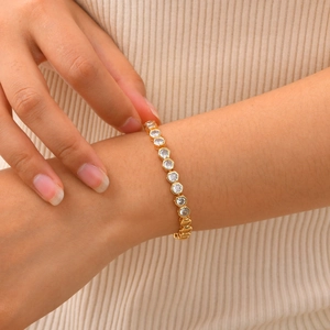Detailed close-up of golden hexagon bracelet with zircon stones on a soft fabric background
