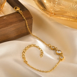 Detailed close-up of gold chain bracelet with three white zircons on soft satin