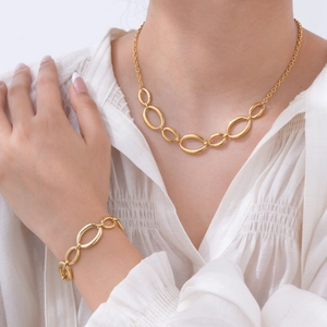 Close-up of a model wearing a gold oval link necklace and bracelet set on a white top