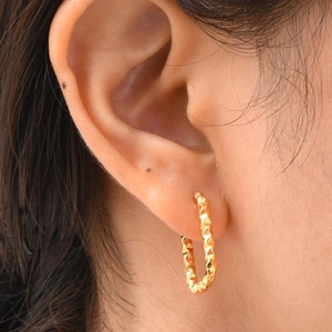 Gros plan de boucles d'oreilles créoles dorées géométriques avec facettes texturées