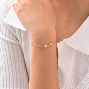 Golden stainless steel cross chain bracelet with white cubic zirconia worn on wrist
