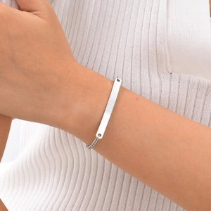 Polished silver stainless steel bar bracelet on model's wrist with minimalist chain