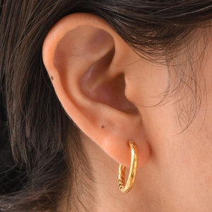 Gros plan de boucles d'oreilles créoles dorées en acier avec motif losanges sur l'oreille