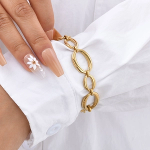 Detailed view of polished gold oval link chain bracelet on a white shirt sleeve