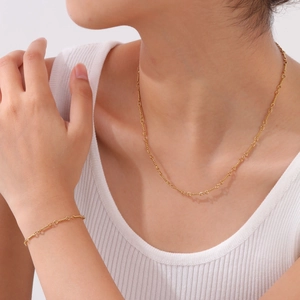 Minimalist gold twisted link bracelet and necklace set worn by a model on white background