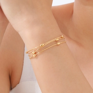 Close-up of triple-layered gold snake chain bracelet with metal beads on female wrist