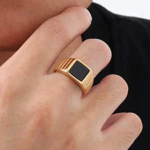 Gros plan d'une bague en acier doré avec pierre noire carrée et anneau à rainures