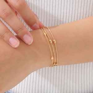 Close-up of golden triple-layered chain bracelet with polished oval beads on wrist