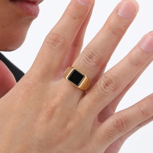 Gros plan d'une bague en acier doré avec pierre d'agate noire carrée sur un doigt