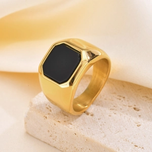 Détail d'une bague chevalière dorée avec pierre d'onyx noire sur un socle en pierre