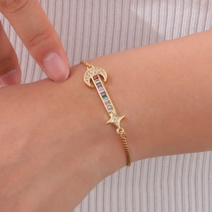 Détail d'un bracelet doré ajustable avec zircons arc-en-ciel et breloques lune et étoile