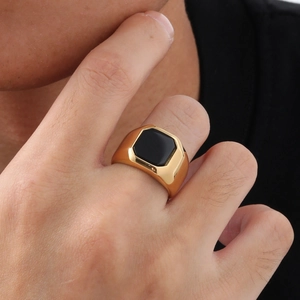 Détail d'une bague géométrique en acier doré avec insert d'onyx noir de forme carrée